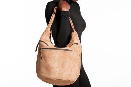 Large suede bucket bag in camel-colored calf-skin leather worn over shoulder, featuring adjustable straps and sleek design against black outfit