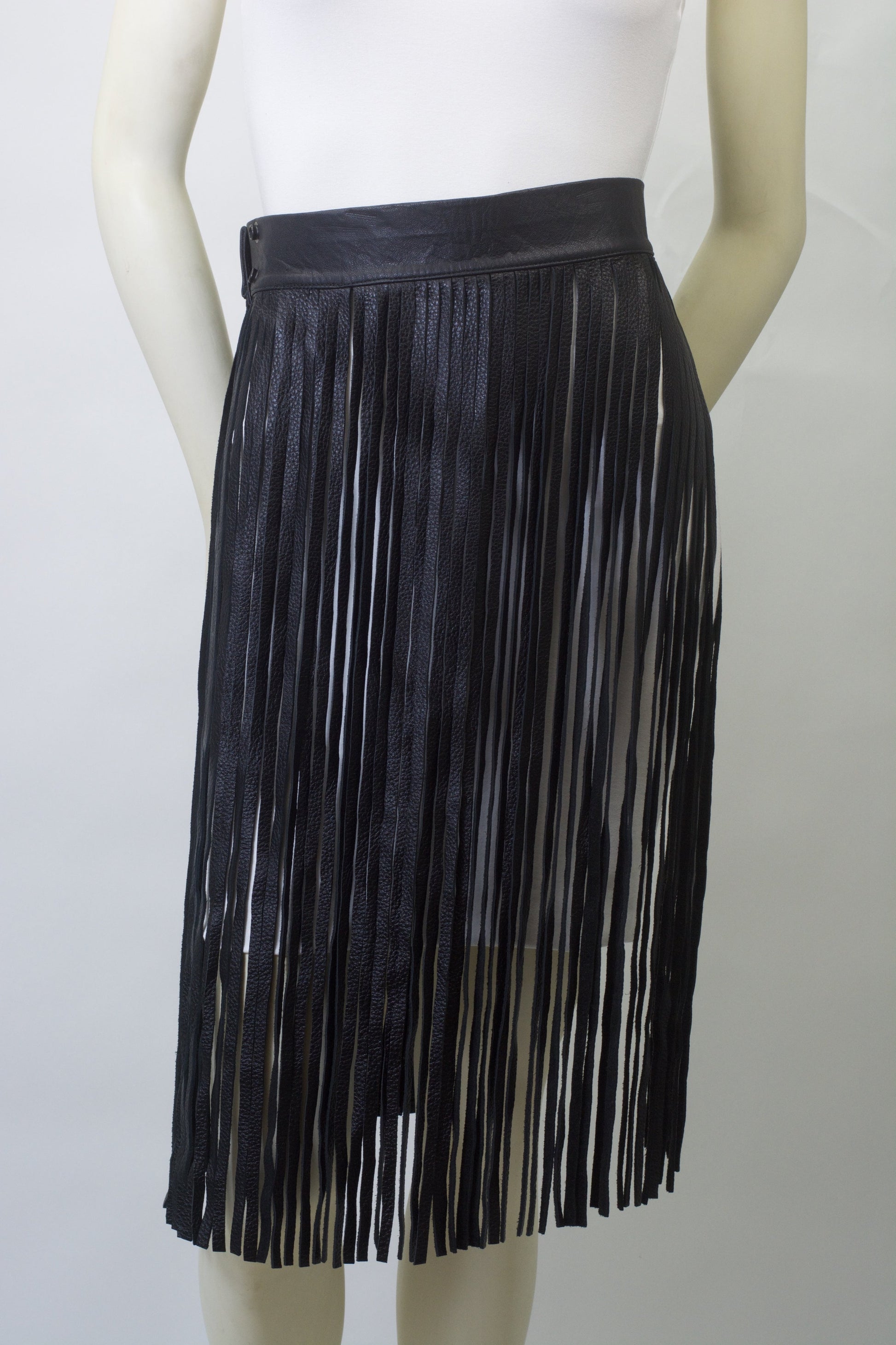 Black leather fringe belt with long flowing fringe detail worn at waist over white top on mannequin, showing adjustable buckle and premium construction.