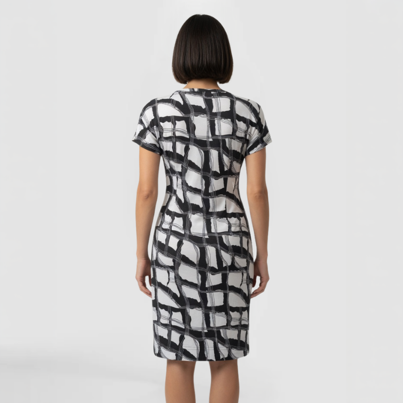 A model poses facing away from the camera in a distinctive black and white patterned dress, knee-length and short sleeves. Made by SWABY- A New York Fashion Designer.