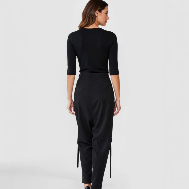 Rear view of model in SWABY Takara Pants in black showcasing draped back detail with ties, smooth fit through hips and legs, side pockets, and structured yet fluid silhouette emphasizing premium fabric and refined modern detailing.