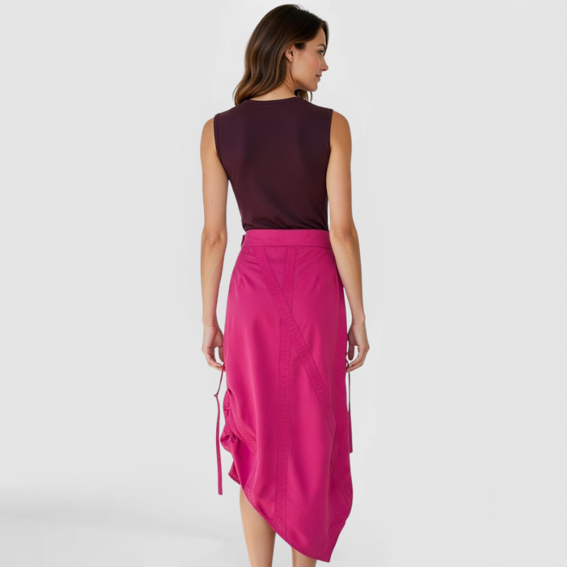 Rear view of model in SWABY Architect Skirt in fuchsia showcasing smooth back with angular seaming detail and side ties; high-waist fit through hips, fluid drape to midi hem, emphasizing premium fabric and modern structural lines.