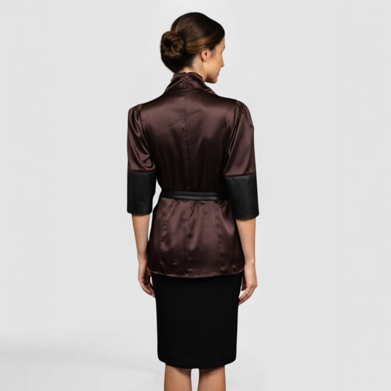 A SWABY fashion model poses, facing away from the camera in a sophisticated burgundy satin turtleneck top with draped cowl collar, subtle puff shoulders, contrasting black faux-leather three-quarter sleeves, and black tie belt cinching the waist, styled over a black pencil skirt for a polished, professional look.