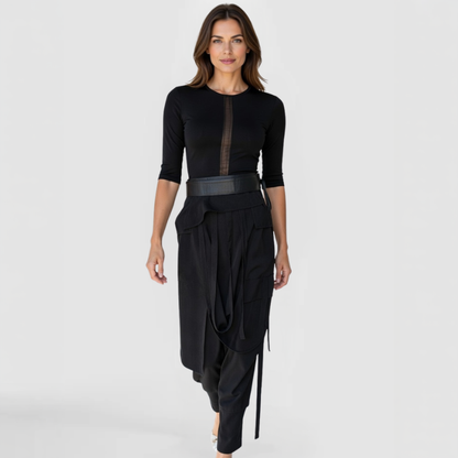 Front view of model wearing SWABY Takara Pants in black; high-waisted design with draped overlay, asymmetric ties, cargo-style pockets, side zipper closure, and relaxed tapered legs for wrinkle-resistant comfort and artistic sophistication.